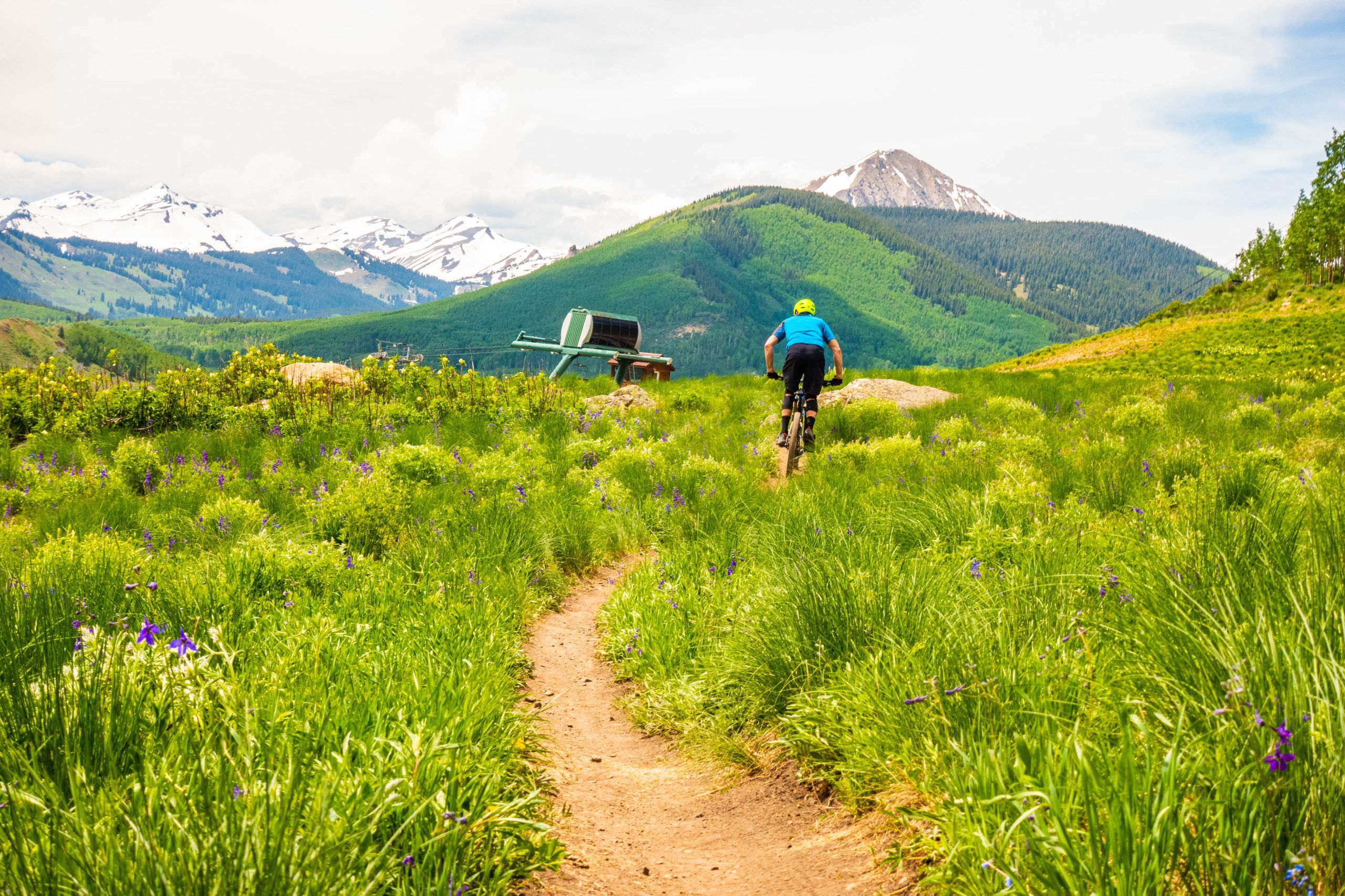 A mountain biker on a trail with the top of a ski lift. MTB crested butte mountain resort in crested butte, co