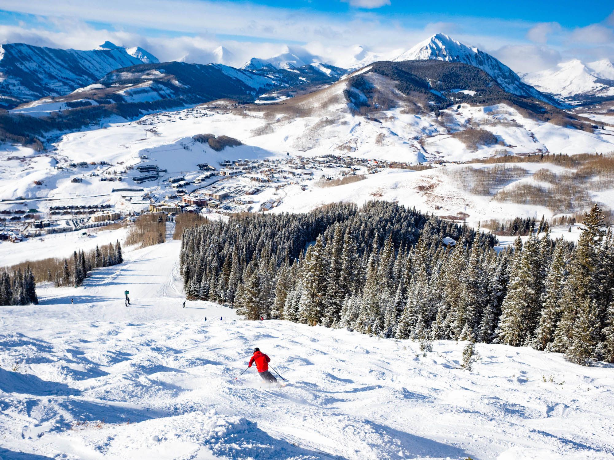 A downhill skier heads down moguls with mountain peaks in the background