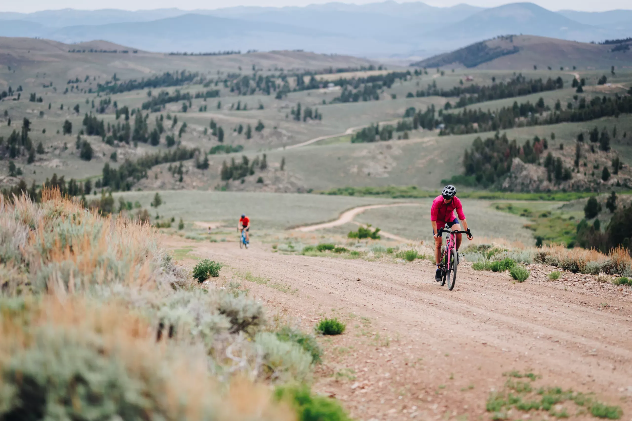three gravel bikers ride on a gravel trail with rolling hills in the background