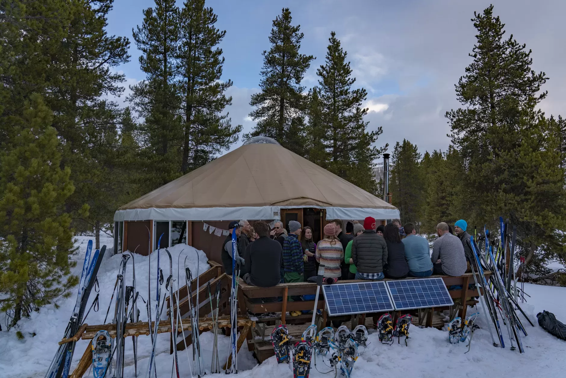 A group of people stand on the deck of a small round building. It is snowy and skis are on a ski rack