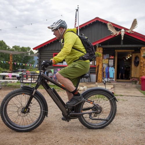 A person riding a bike in front of a rural gunnison county lodging in pitkin. The building is log cabin-style and has mouse antlers mounted above the door