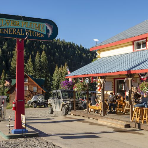 A sign that says "Silver Plume General Store" in front of a building with picnic tables that people are eating at outside in Pitkin, Colorado