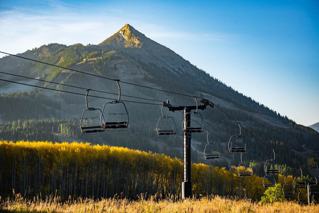A ski lift hanging above fall trees. A mountain peak is in the background.