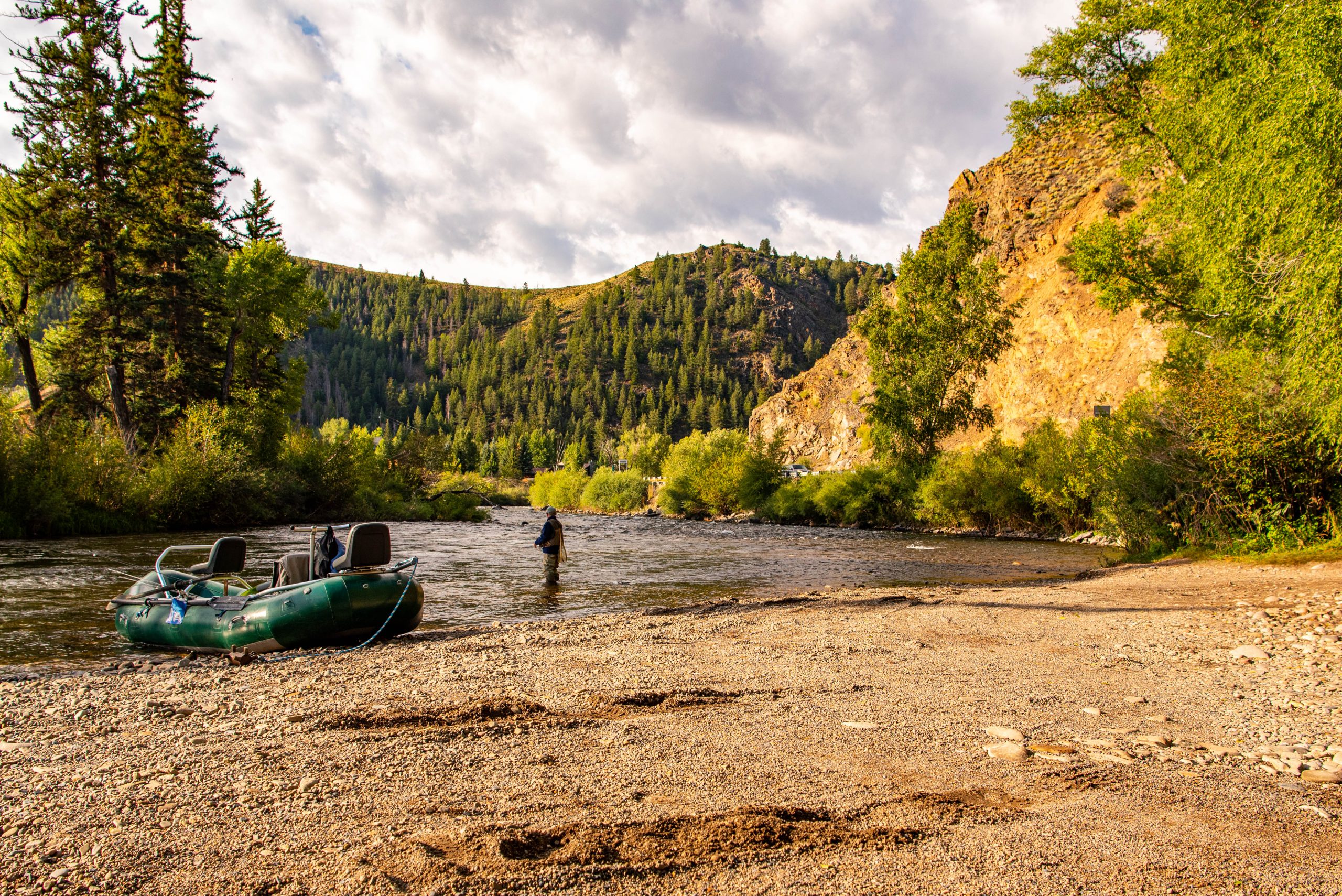 Whitewater Rafting the Gunnison River a fisherman wades into a river with his raft nearby.