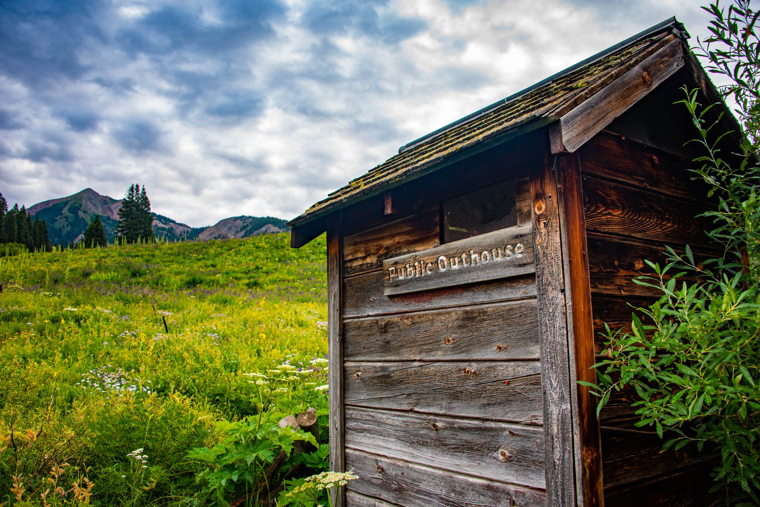 An old wooden cabin in a field of green grass with a blue and cloudy sky