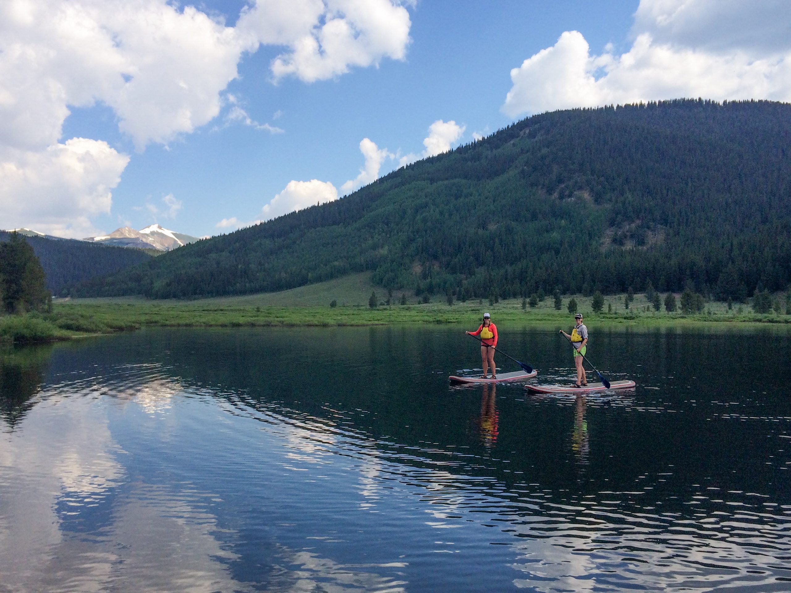 Crested Butte Stand-up Paddleboarding two women wearing life jackets paddle across a lake on SUPs.