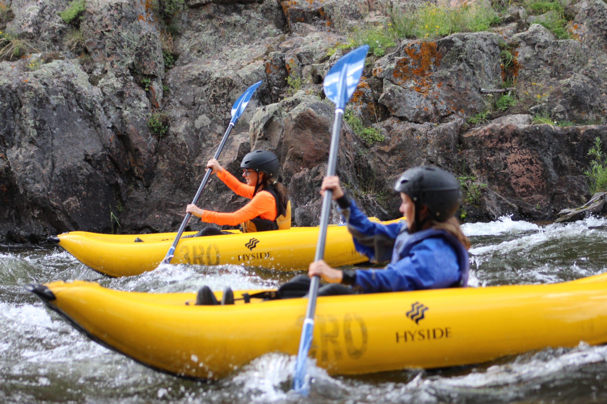 Kayaking Crested Butte two women paddle yellow duckies on a river through a gray rock canyon.