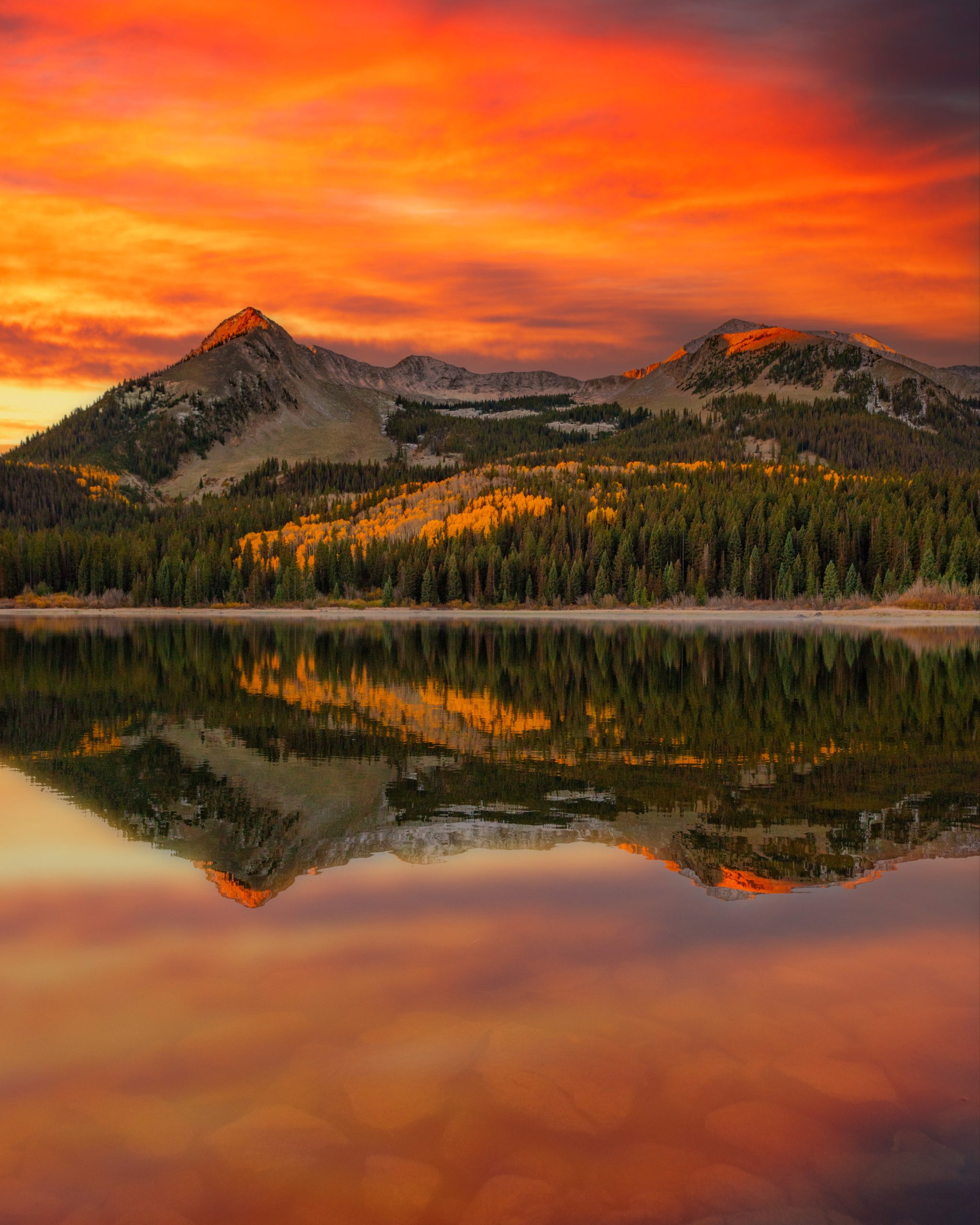 A pointy mountain peak reflected back in a lake and lined by trees. Lost Lake sunrise sky reflection. 