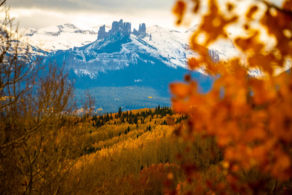 Fall colors in Colorado blurred out in the foreground with a peak that looks like castles in the background