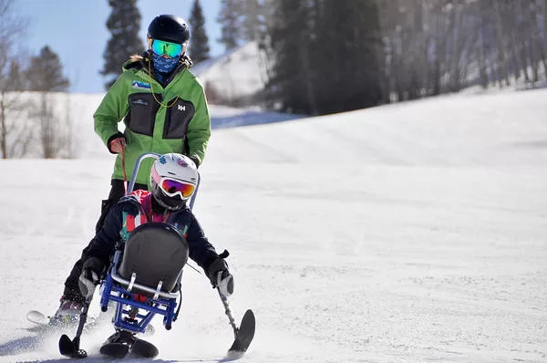 A volunteer helps an adaptive skier ski down a run