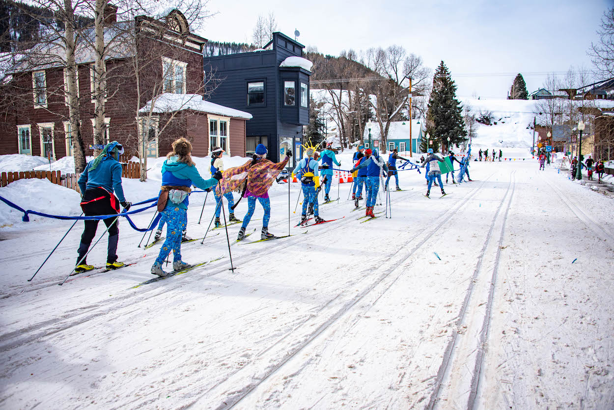 Nordic skiers race in two lines dressed in costumes on a snowy downtown street