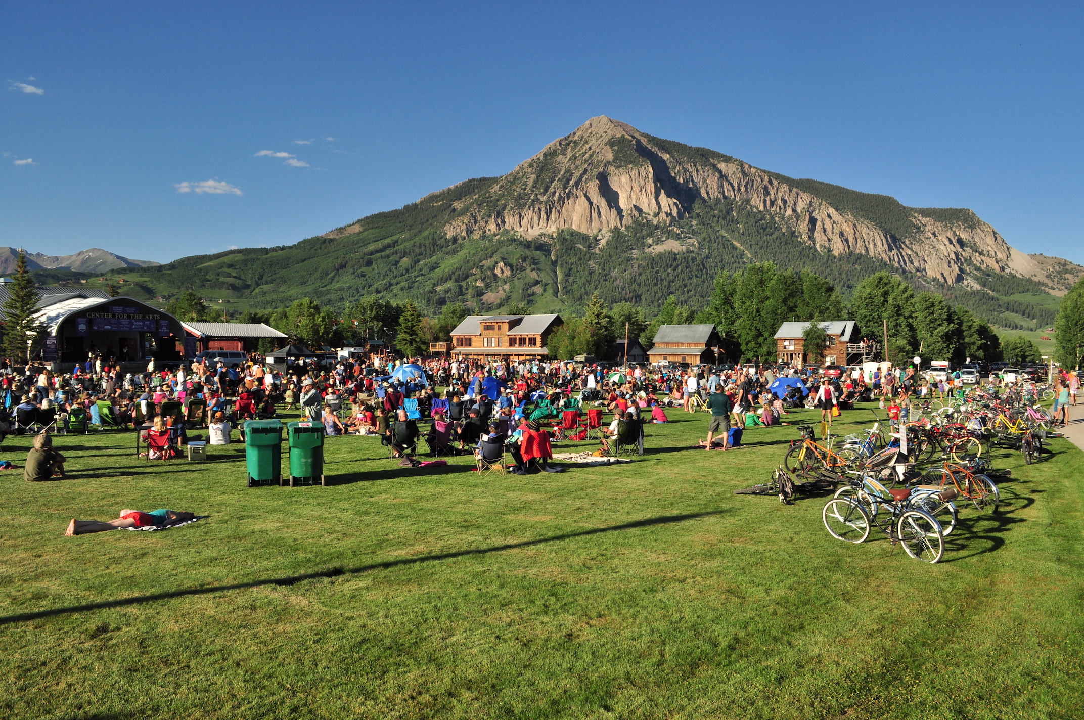 A lawn full of people sitting on chairs and blankets with a mountain peak in the background.