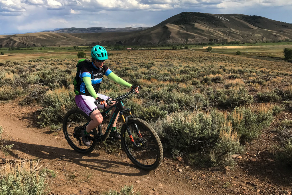 Beginner MTB trails in Crested Butte a female mountain biker rides on a smooth trail through sagebrush. Tenderfoot Mountain is in the background. It is summer.