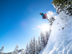 A skier jumps off a cliff in Big Chute at Crested Butte on a sunny winter day.