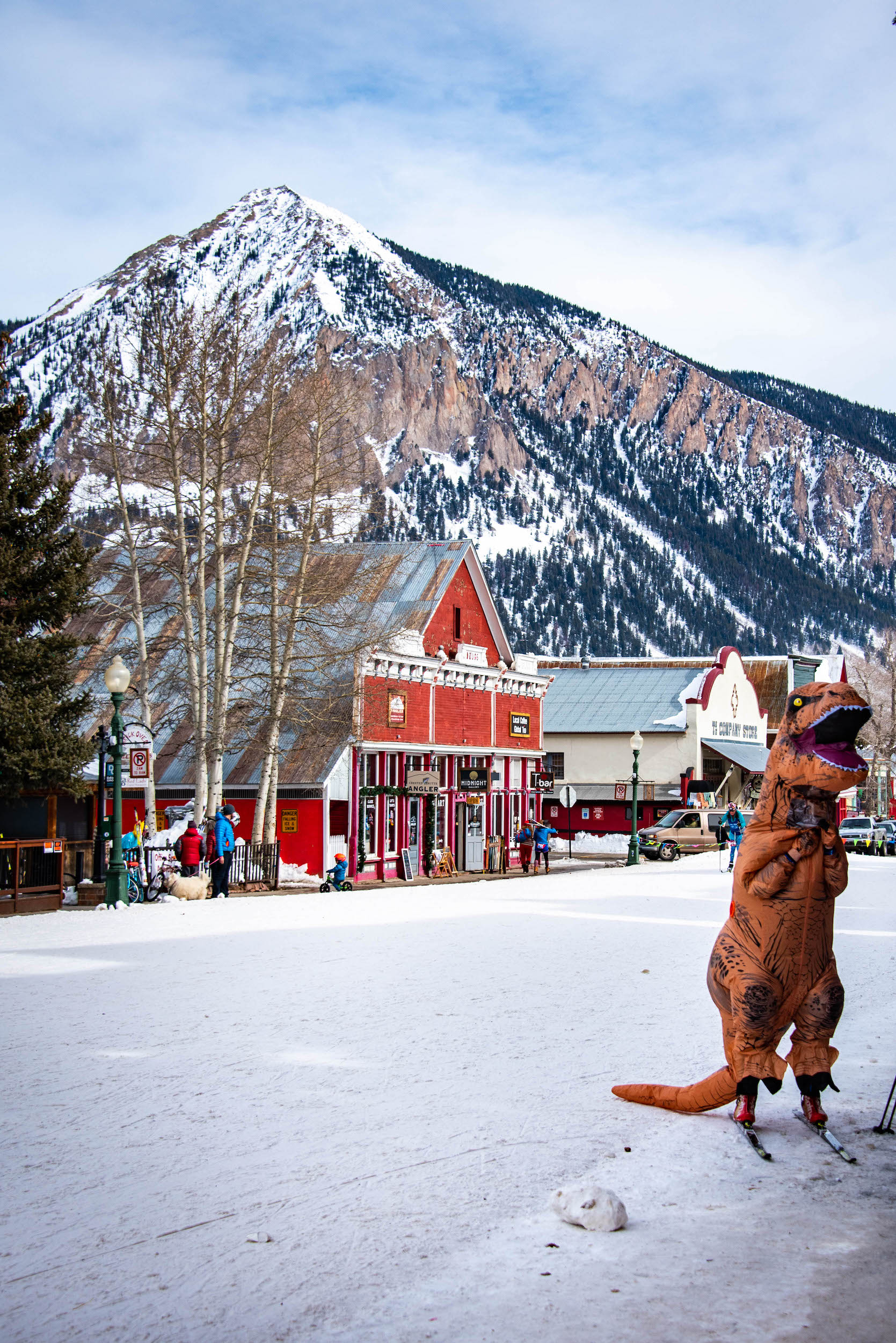 A person dressed in a dinosaur costume and wearing skis on a downtown street for the Crested Butte Alley Loop