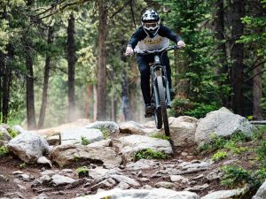A mountain biker in a full-face helmet rides through a rock garden on the Crested Butte Mountain Bike Park Trails.