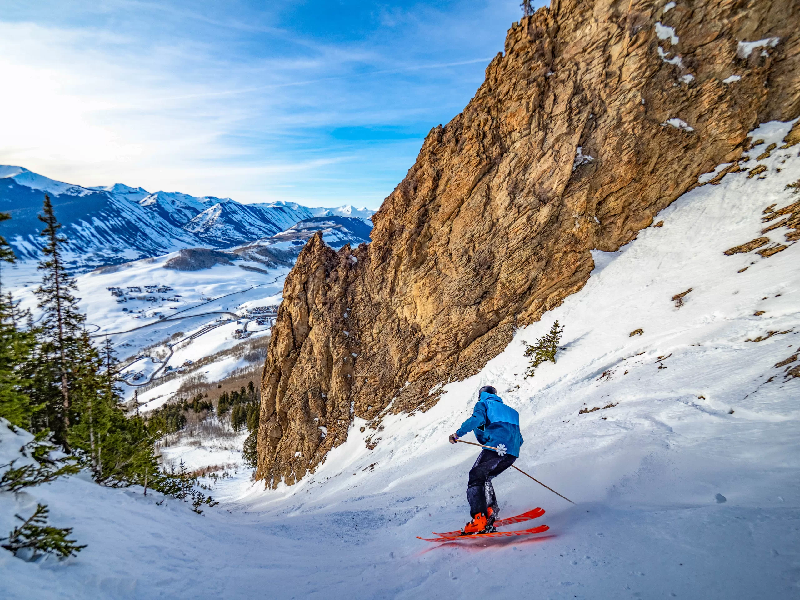 a person skis down a steep chute with snowy peaks in the background