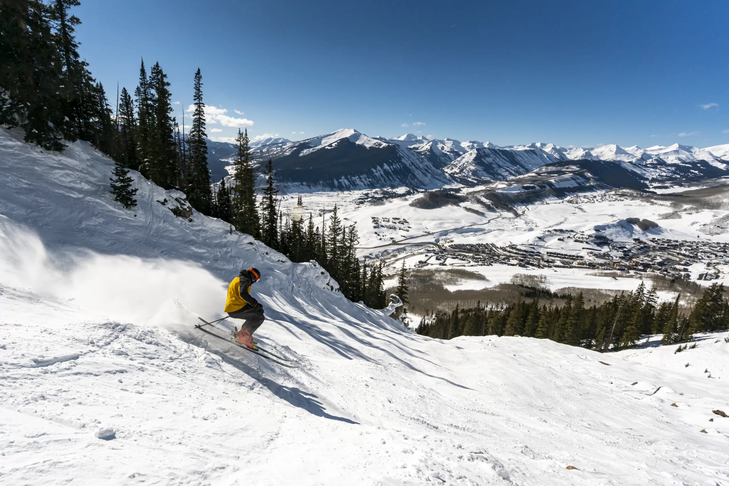 A skier on a steep slope with mountain peaks in the background