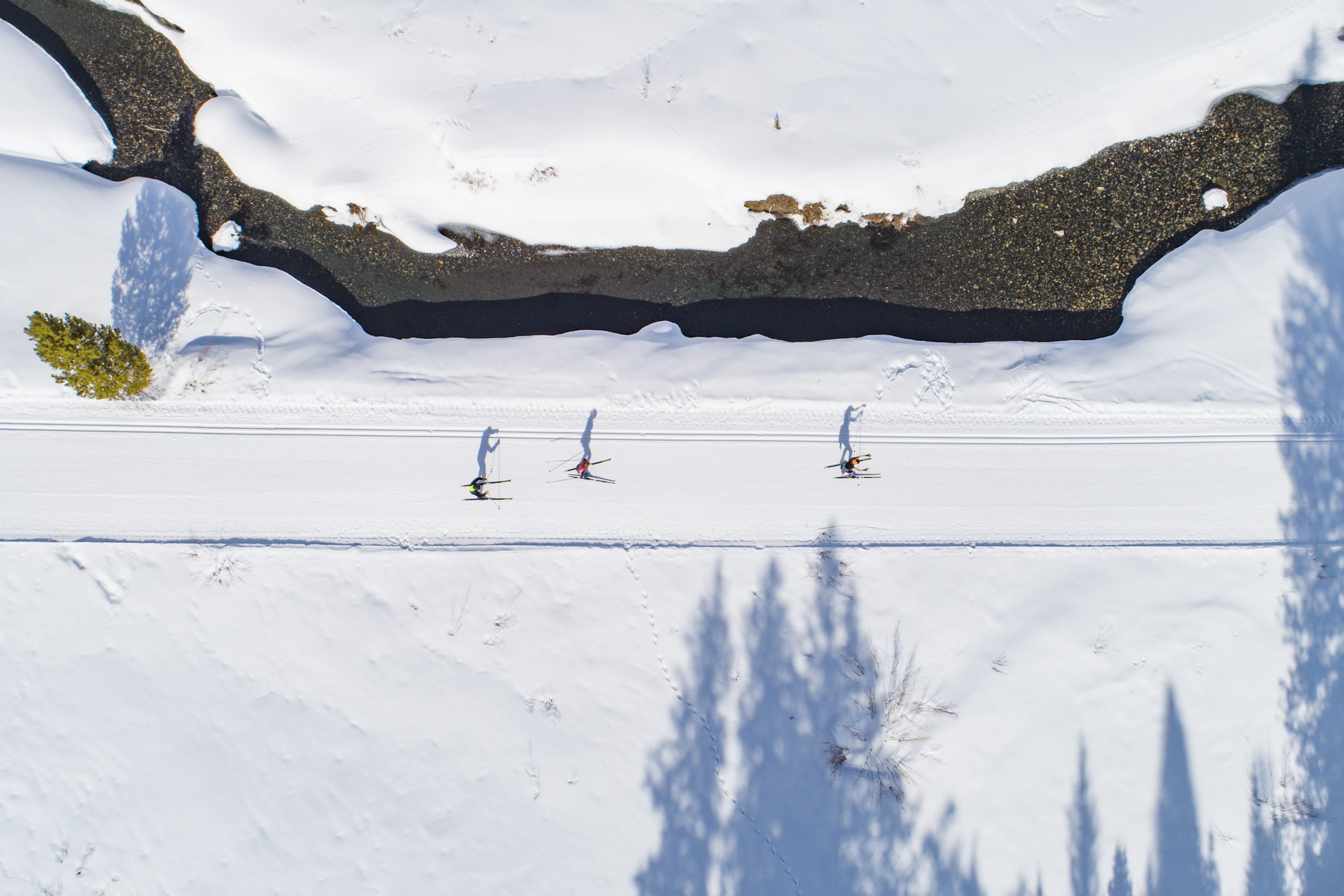An aerial view of cross-county skiers on a groomed track along a stream