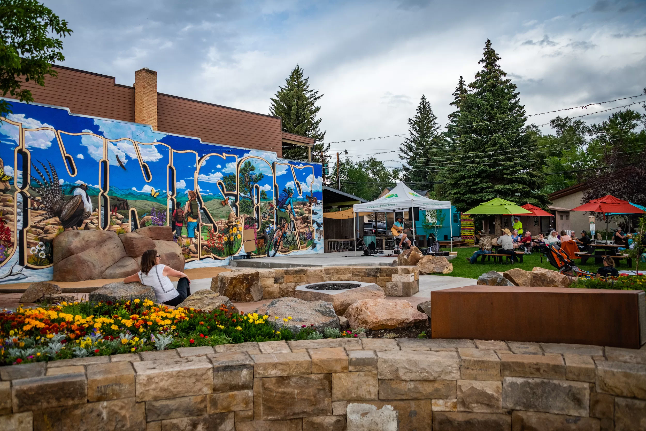 A downtown park with a mural on the wall, tents set up and someone playing music on a stage