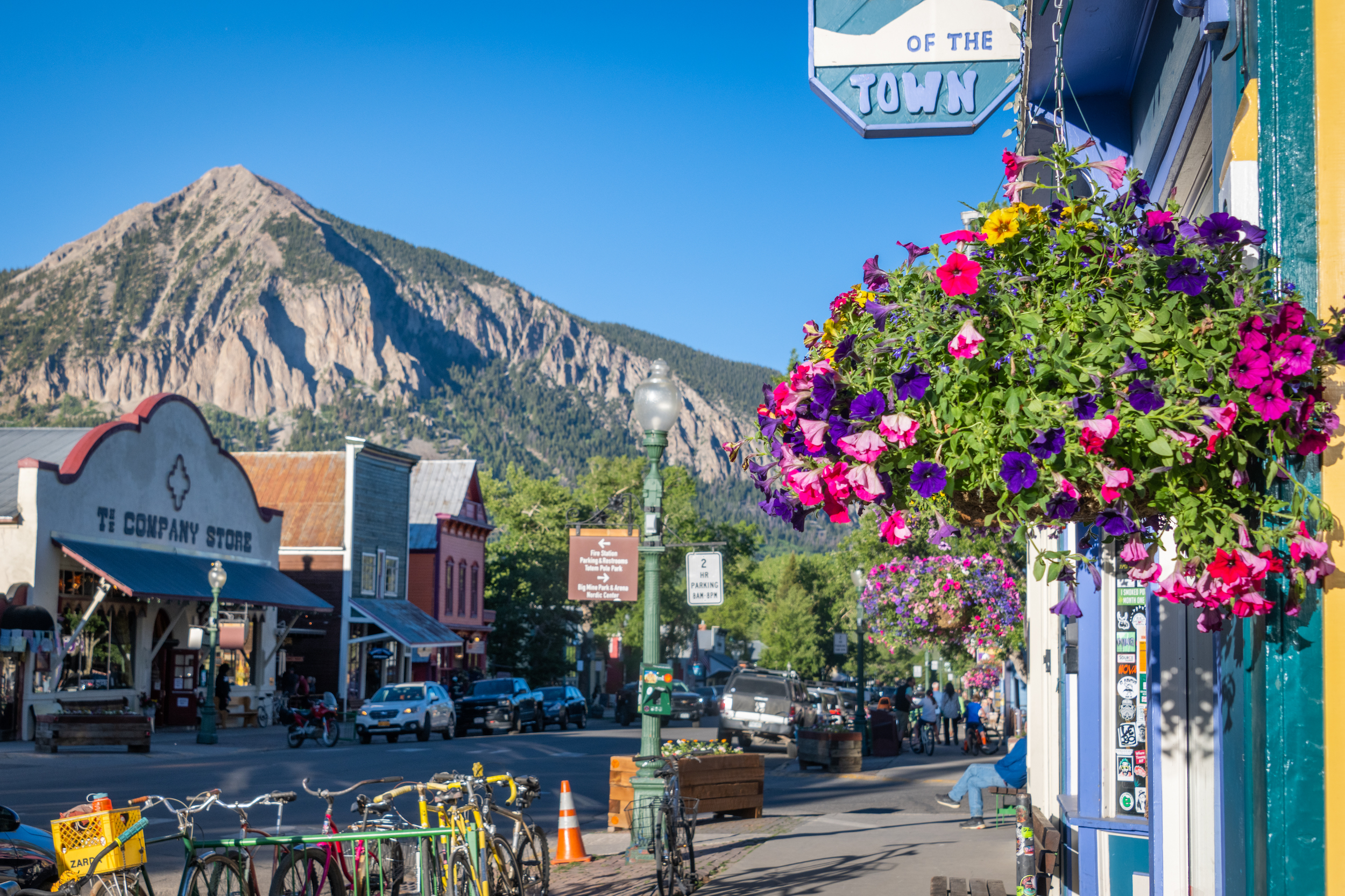 A pointy mountain peak hanging over a downtown street lined with shops, bikes and flower baskets on elk avenue crested butte colorado