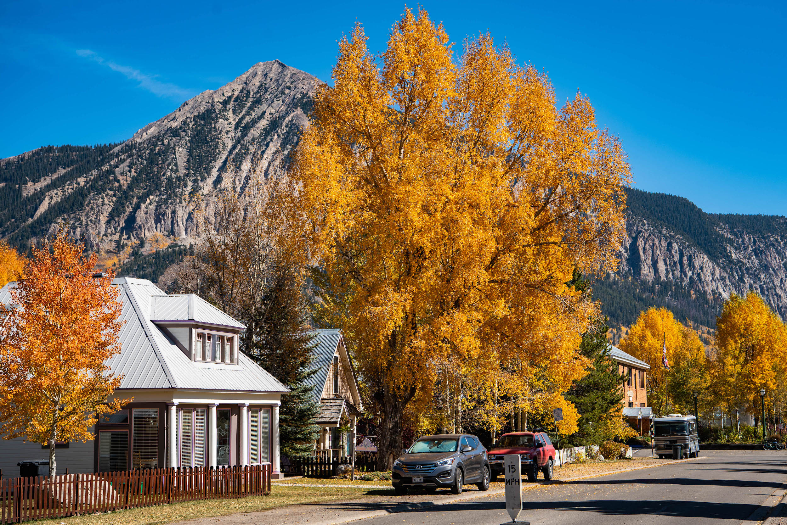 A view of a street with a mountain peak and a tree bursting with fall leaves