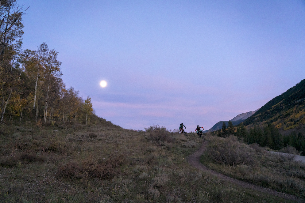 Two mountain bikers riding at dusk. The sky is blue and pink and purple.