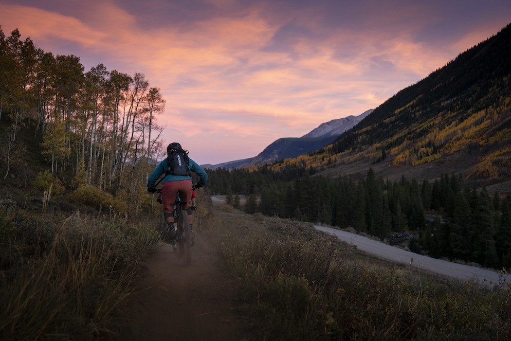 A colorful sunset over a mountain biker riding through yellow aspen leaves
