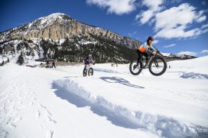 Racers hit the jumps with Crested Butte in the background on a sunny winter day at the Fat Bike World Championships. 