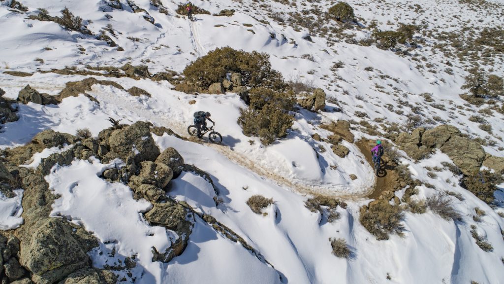 Ah overhead view of people biking in snow on fat bikes. The environment is rocky