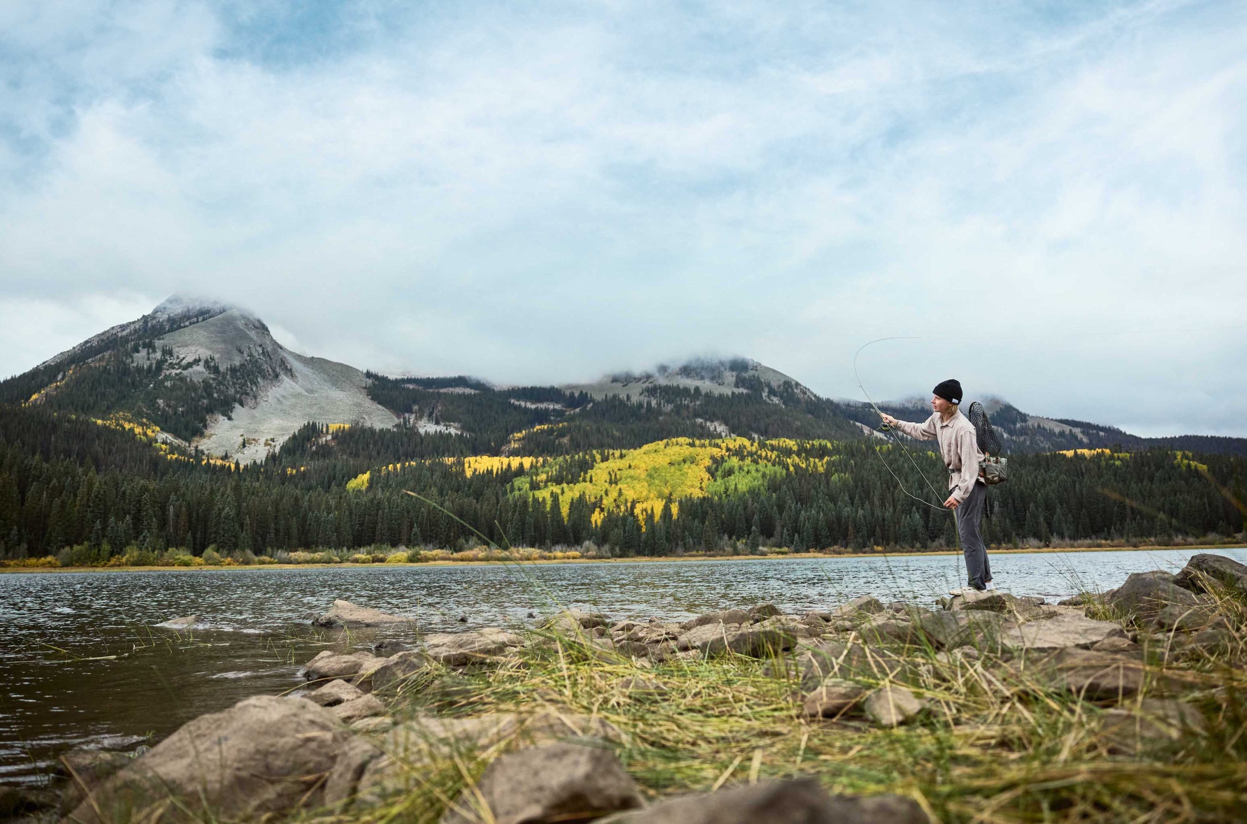 A man fly fishes on the shore of a lake