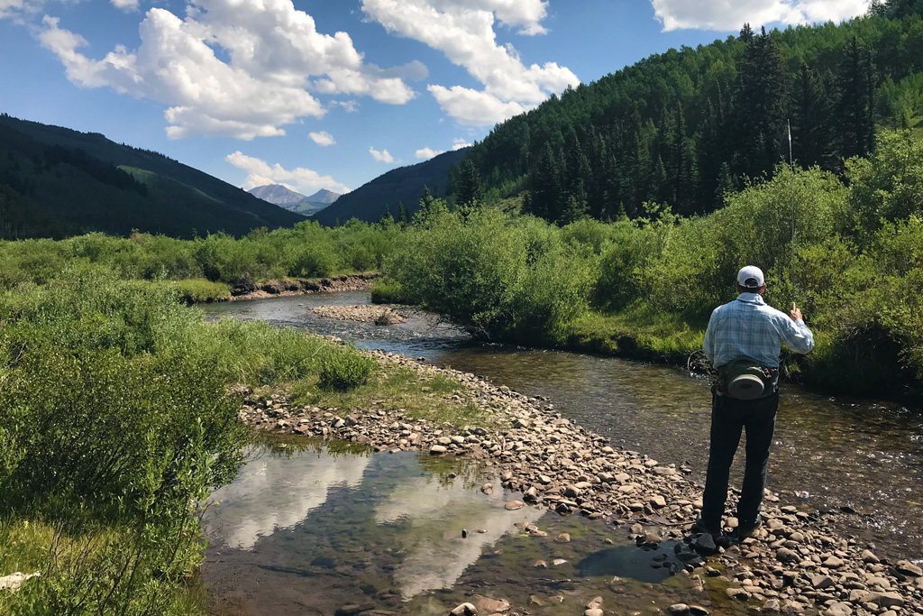 A photo of the back of a fly-fisherman as he casts into a creek in the Gunnison Valley