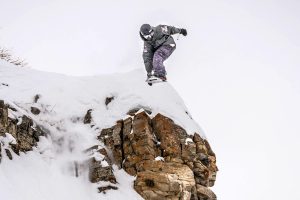 A Western Mountain Sports freeride athlete jumps off a cliff into the snow.