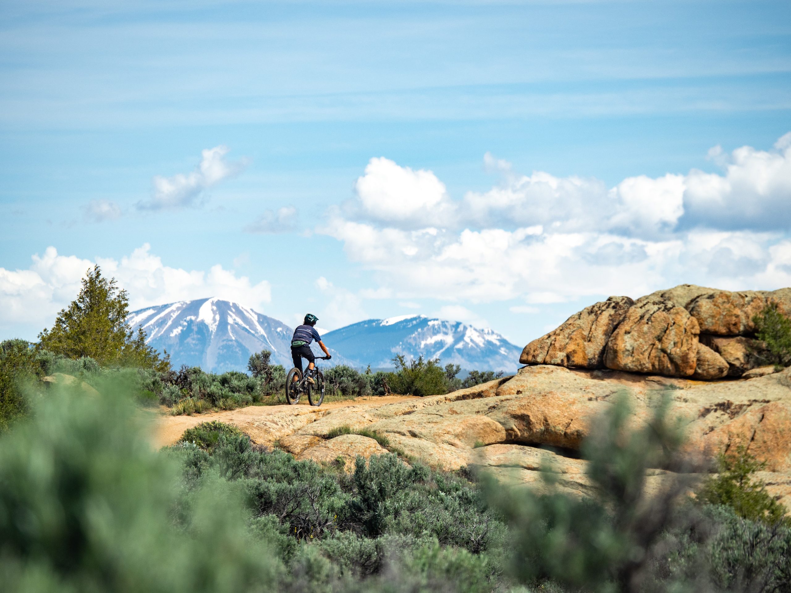 A mountain biker on a rocky trail with snow-capped peaks in the background