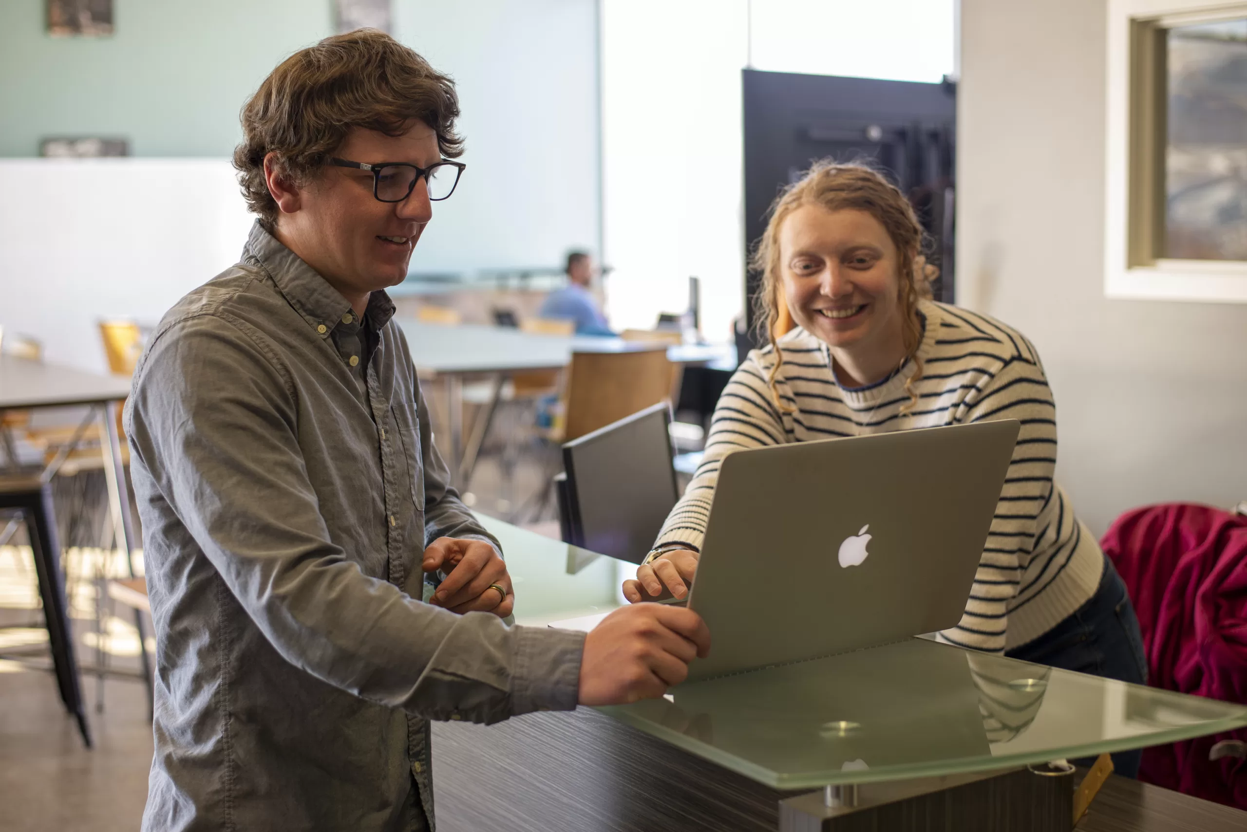 two people look at a laptop computer sitting on a desk