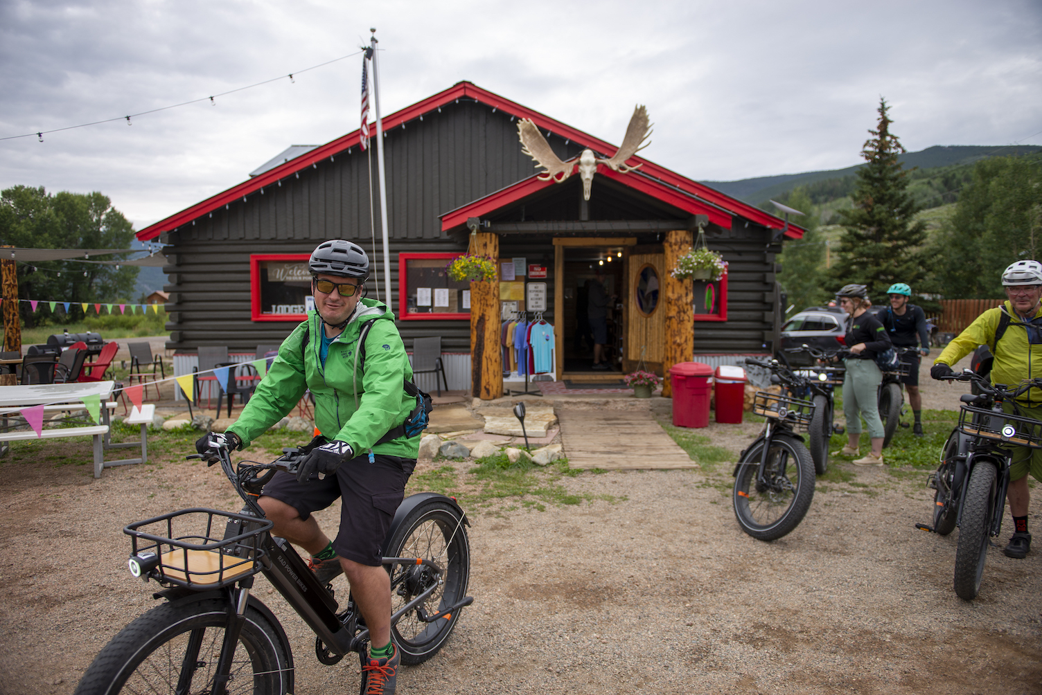 People on bikes in front of a log cabin building with moose antlers mounted above the door. This lodging in pitkin is the stumbling moose lodge