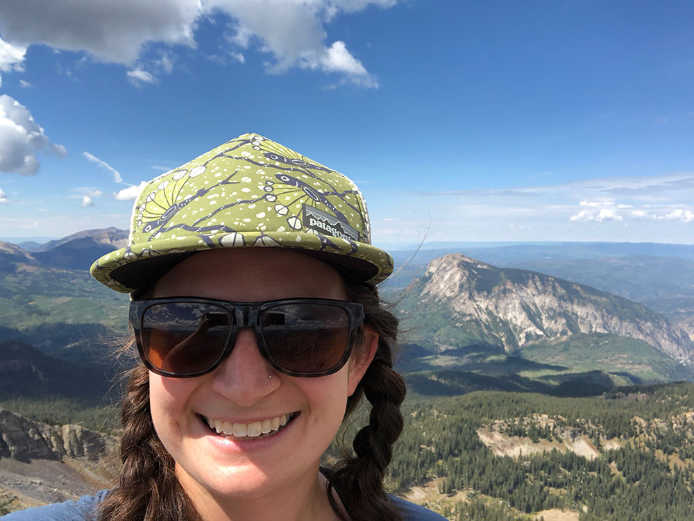 selfie of Mel at the top of a peak near Crested Butte, CO with other mountains in the background