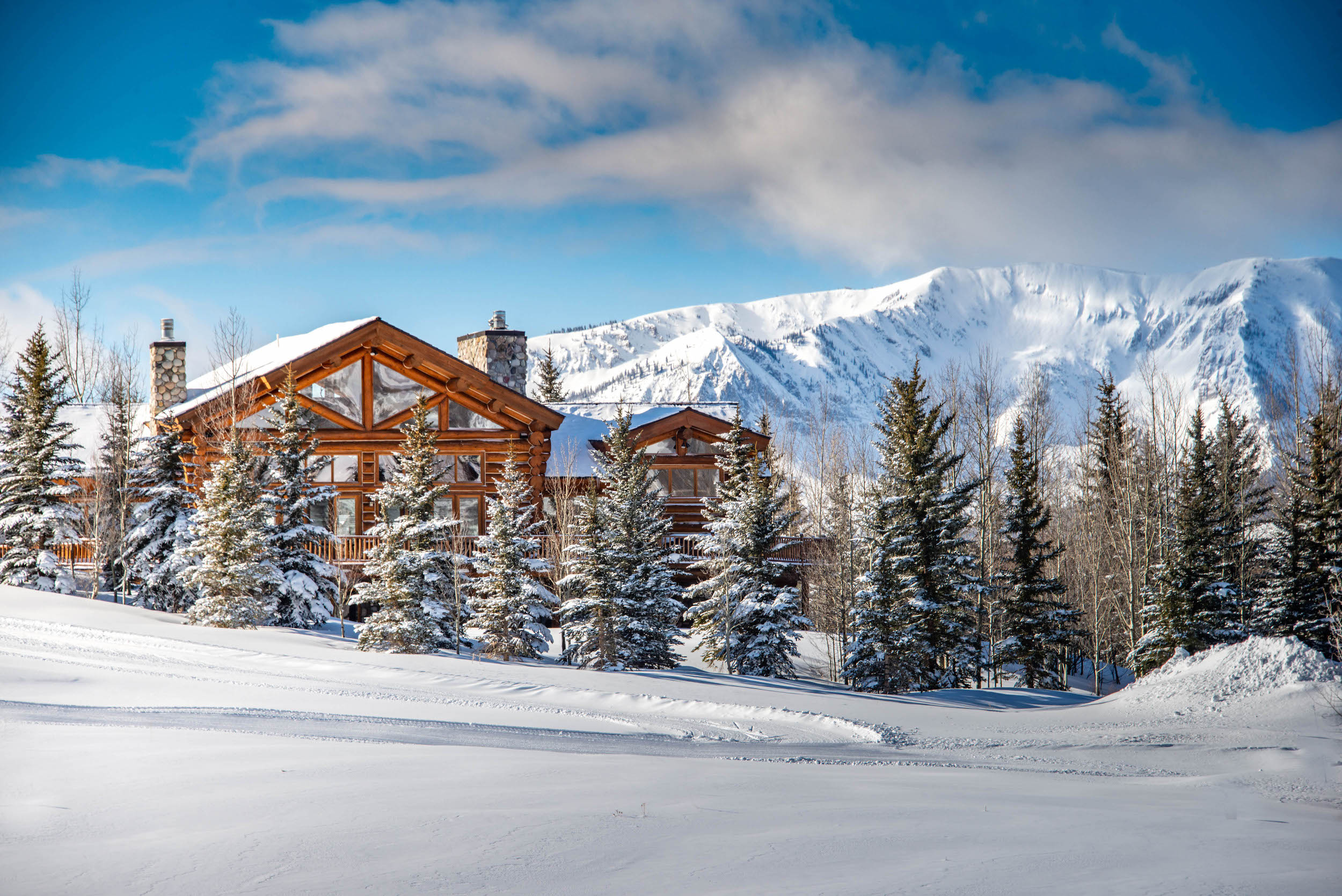 A large home on a snowy hillside with mountains in the background. This is an example of a Mt. Crested Butte lodging property