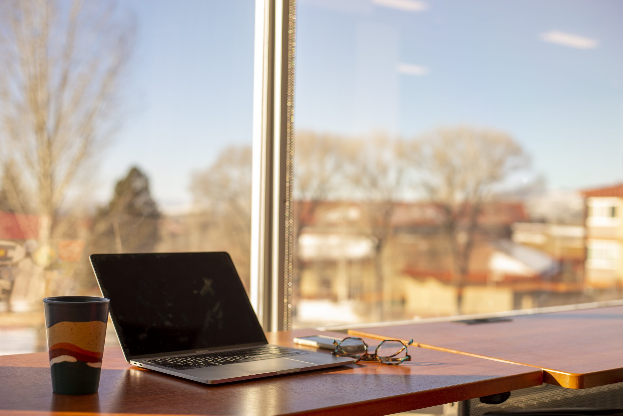 A cup, laptop and pair of glasses on a desk