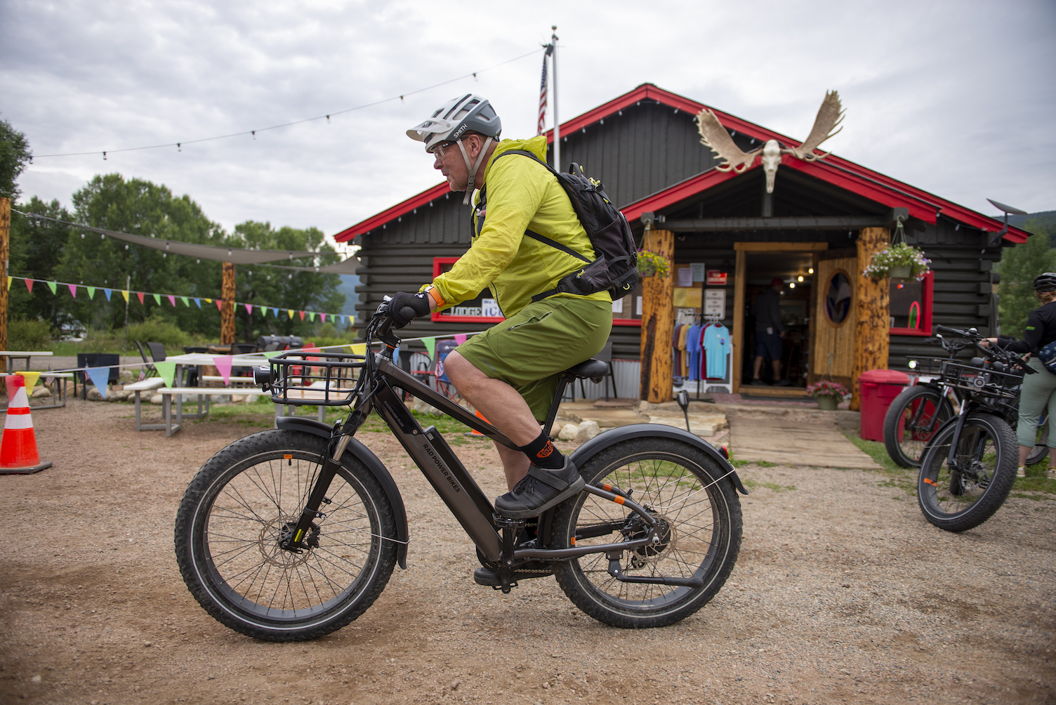 A person riding a bike in front of a rural gunnison county lodging in pitkin. The building is log cabin-style and has mouse antlers mounted above the door