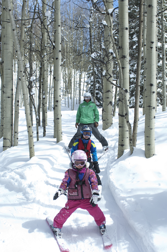 An adult and two children ski on a trail through the trees.