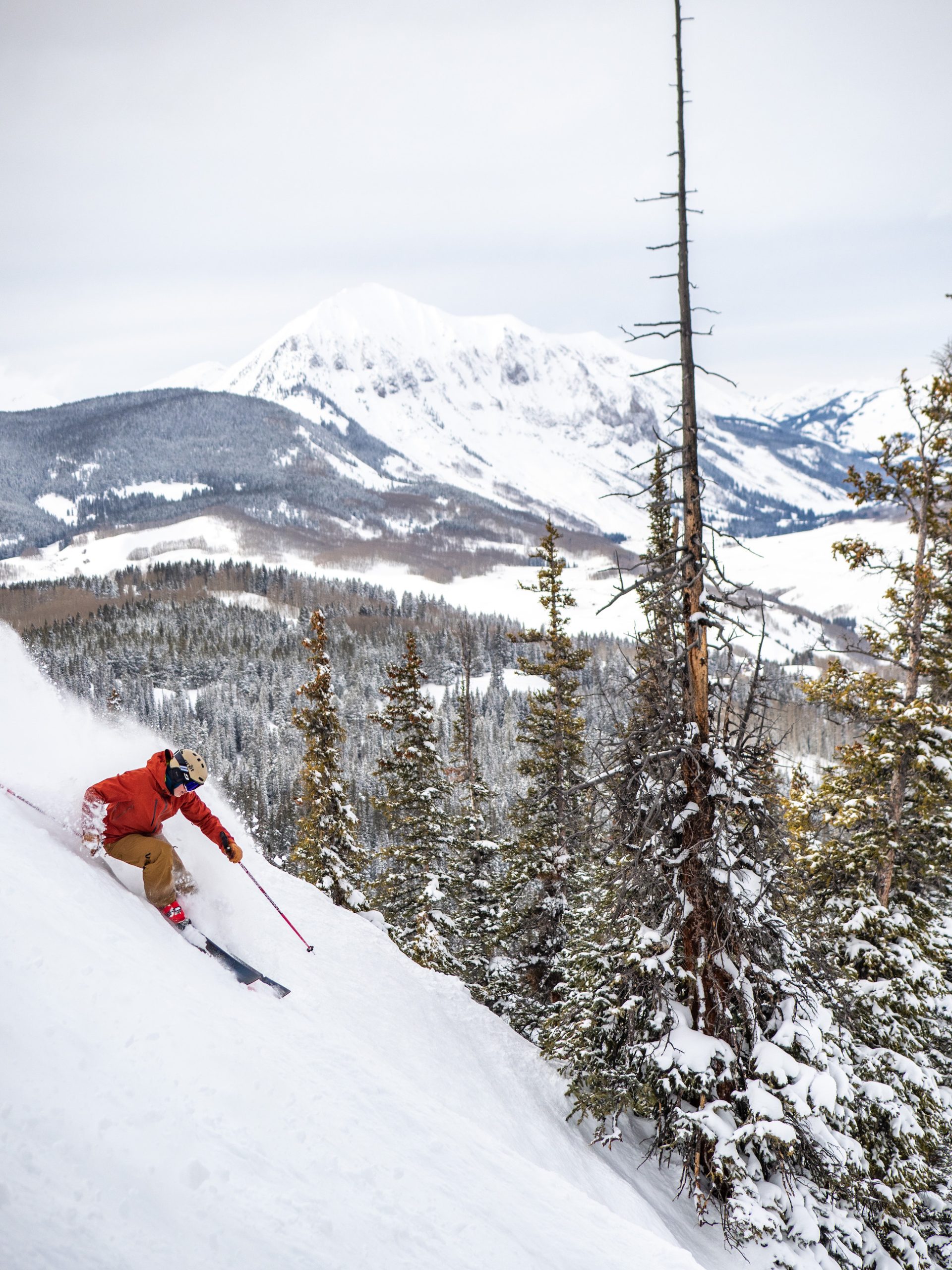 A person skis down a steep slope with a mountain peak in the background. Crested Butte Mountain Resort is known for steep skiing. 