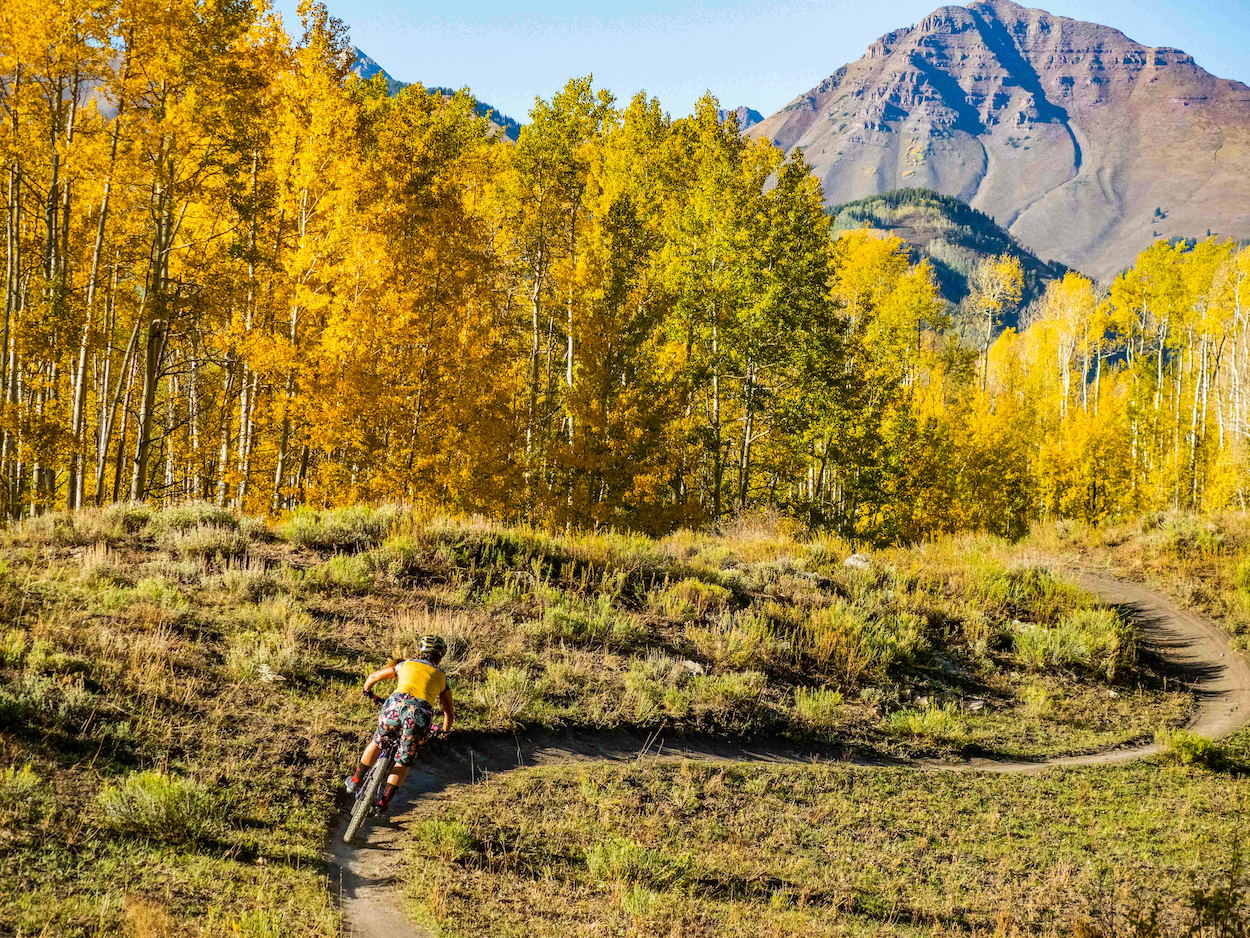 A person riding a mountain bike on a path in front of a mountain peak. This trail is Strand Hill Crested Butte