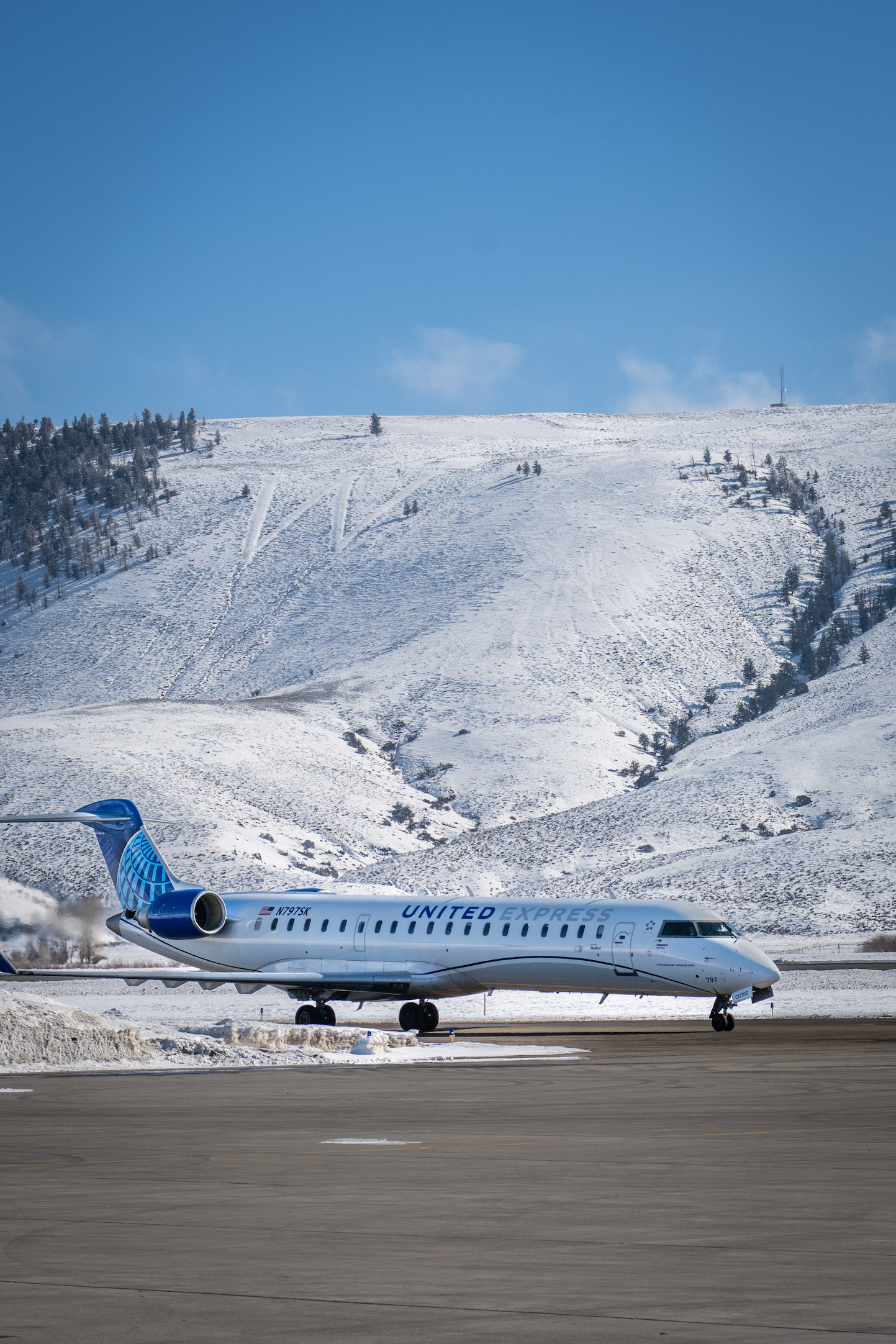 an airplane that says "united" sitting on the tarmac under a snowy hillside with a large capital W at an airport called GUC